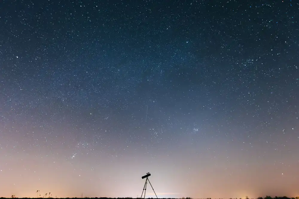 A high-end telescope silhouette against a dramatic starfield